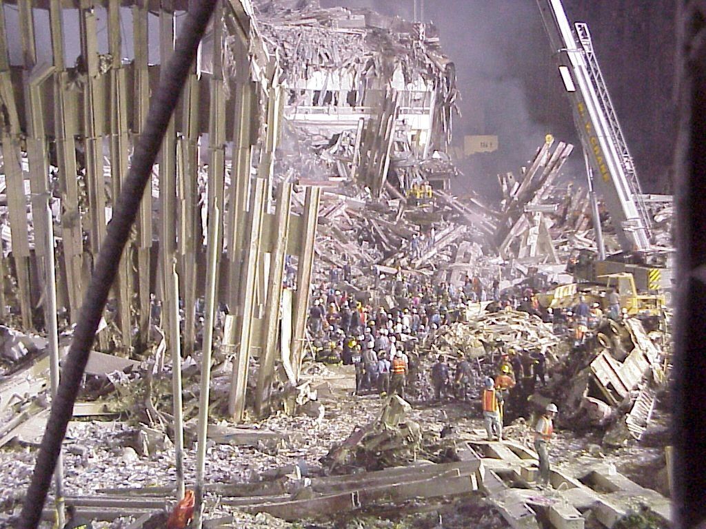 World Trade Center site in 2001: standing sections of the perimeter structure rising above the debris field, with smoke across the scene.