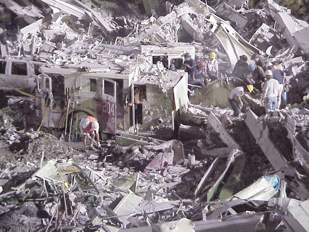 World Trade Center site, 2001: emergency responders in reflective gear at the foot of the debris field at night, with a crane working behind them.